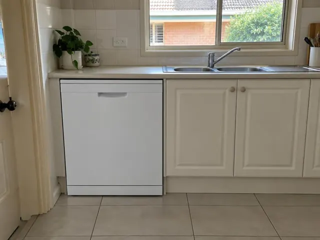 White dishwasher under a kitchen benchtop beside a sink and tiled floor in Loxford