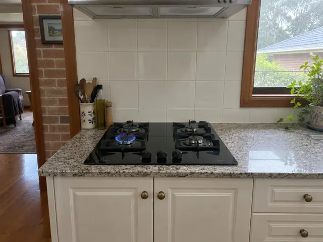 Black gas cooktop set into a speckled benchtop with tiled splashback in a home kitchen in Pelaw Main